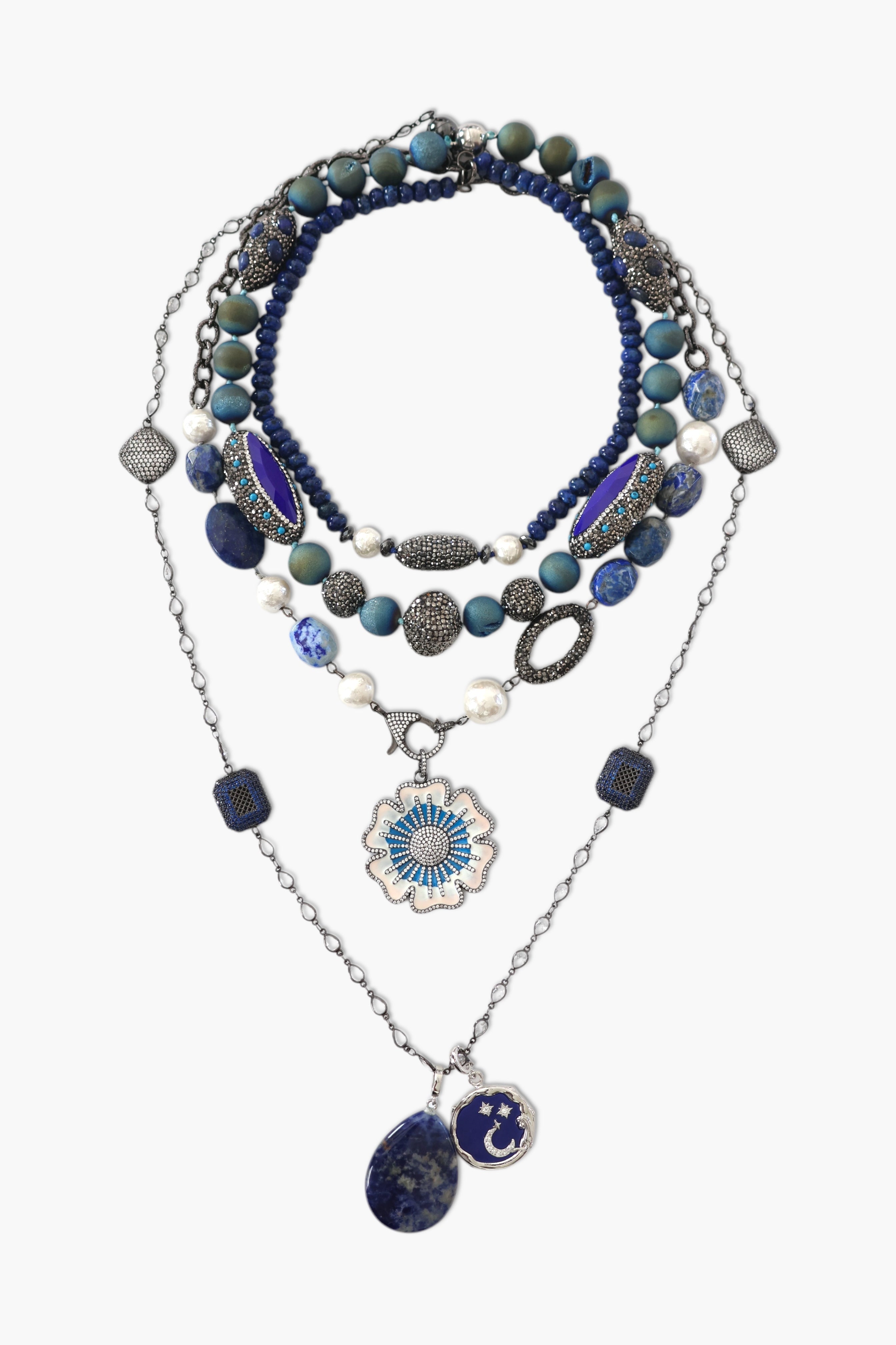 A person wearing a floral shirt and blue jeans, adorned with a stack of blue and gold necklaces featuring lapis lazuli and blue agate.