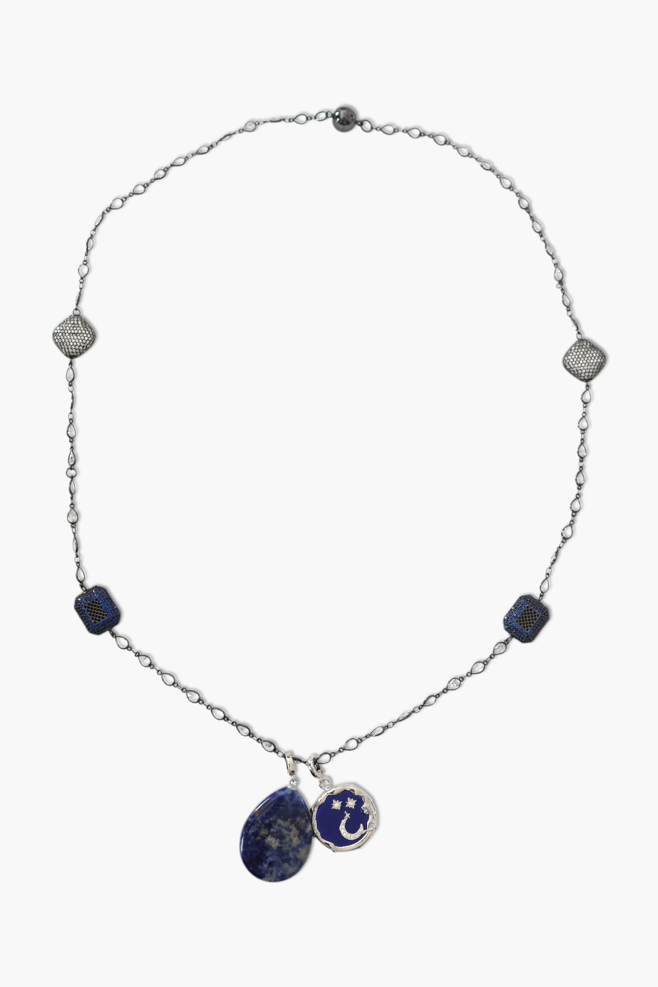 A person wearing a floral shirt and blue jeans, adorned with a stack of blue and gold necklaces featuring lapis lazuli and blue agate.