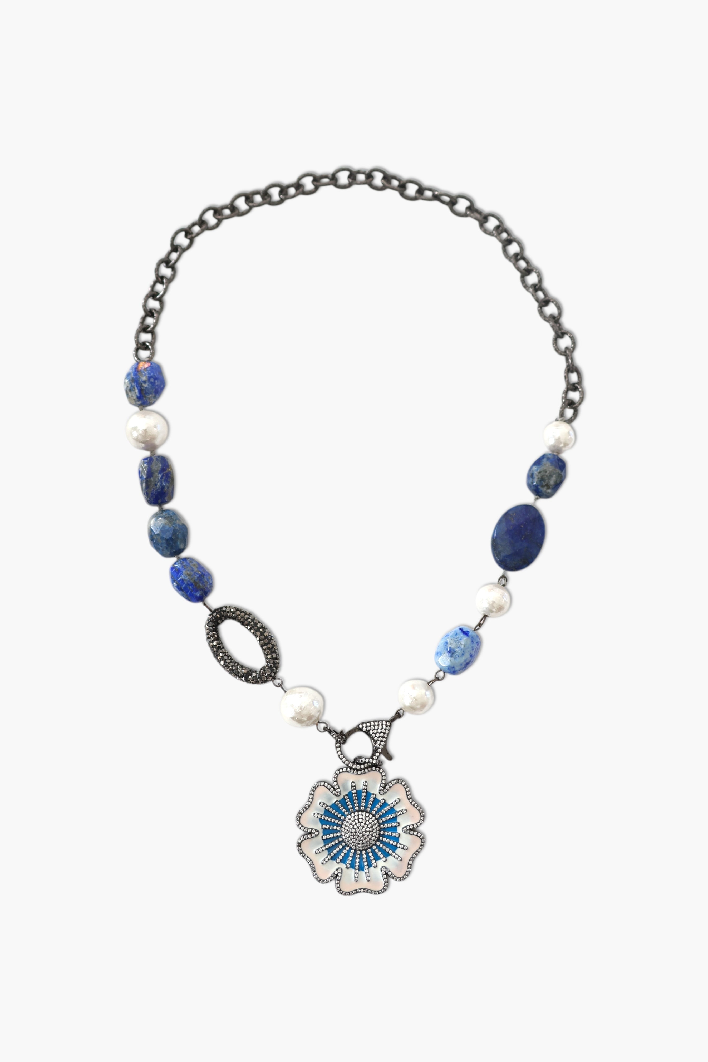 A person wearing a floral shirt and blue jeans, adorned with a stack of blue and gold necklaces featuring lapis lazuli and blue agate.