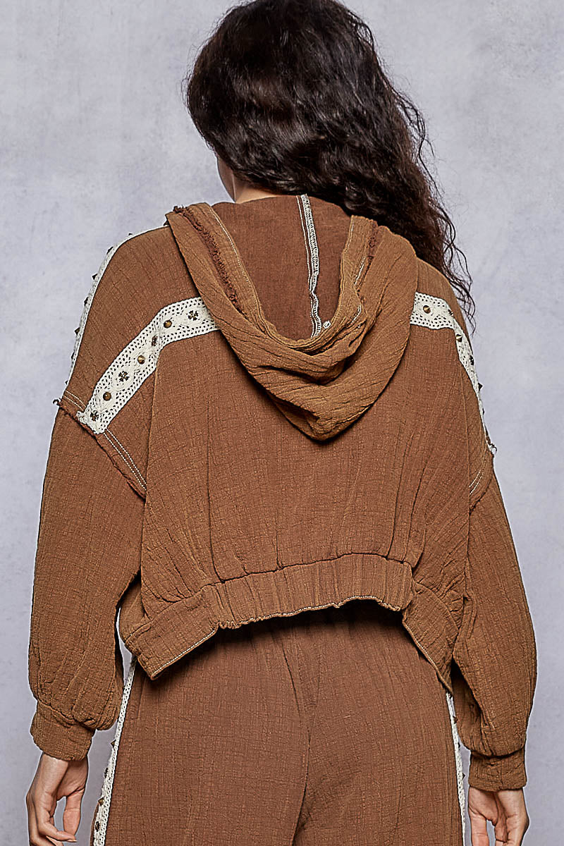 Person wearing a brown hoodie with lace details on a plain background