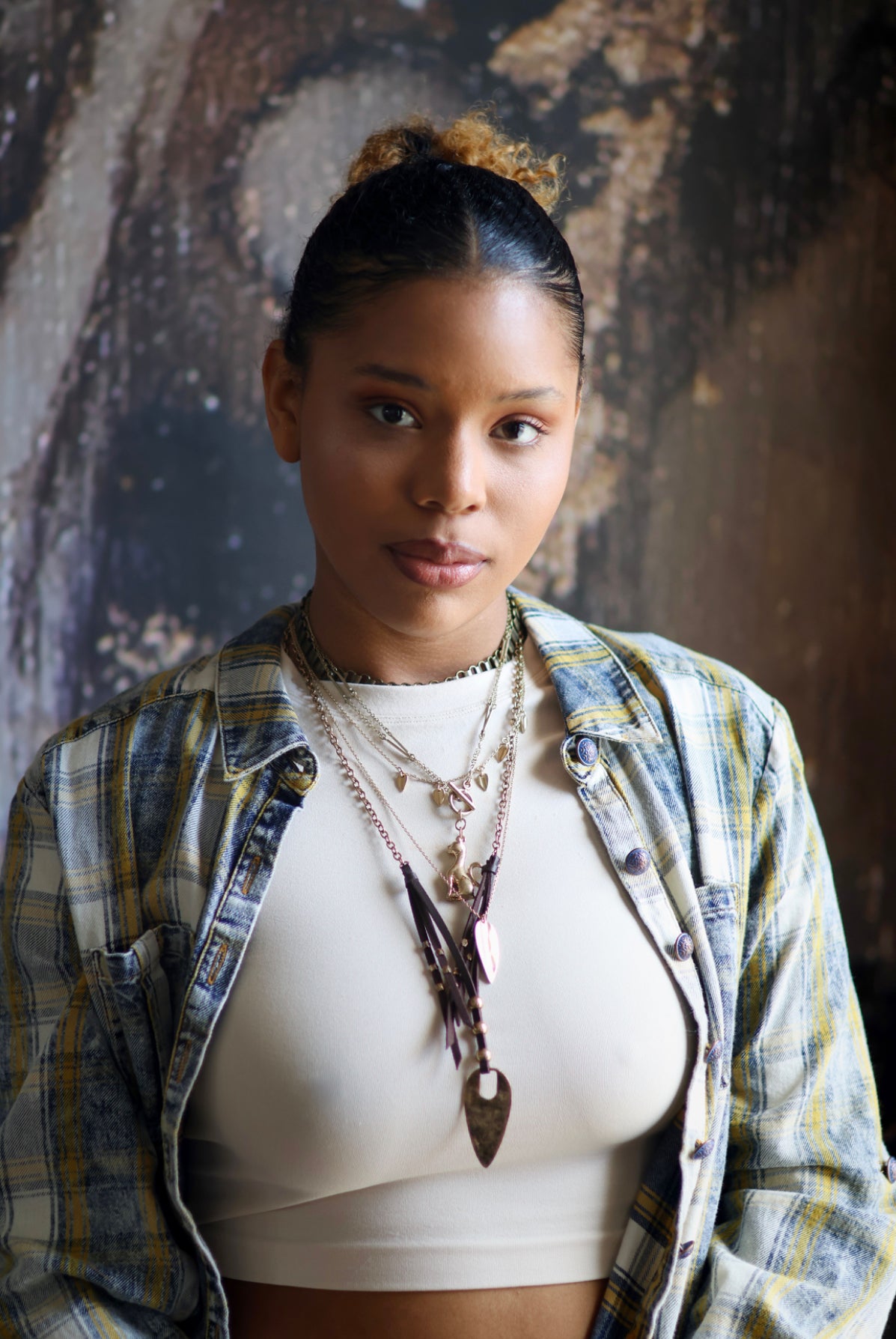 A person wearing a brass necklace with a flowing design, featuring multiple layers and a prominent pendant.