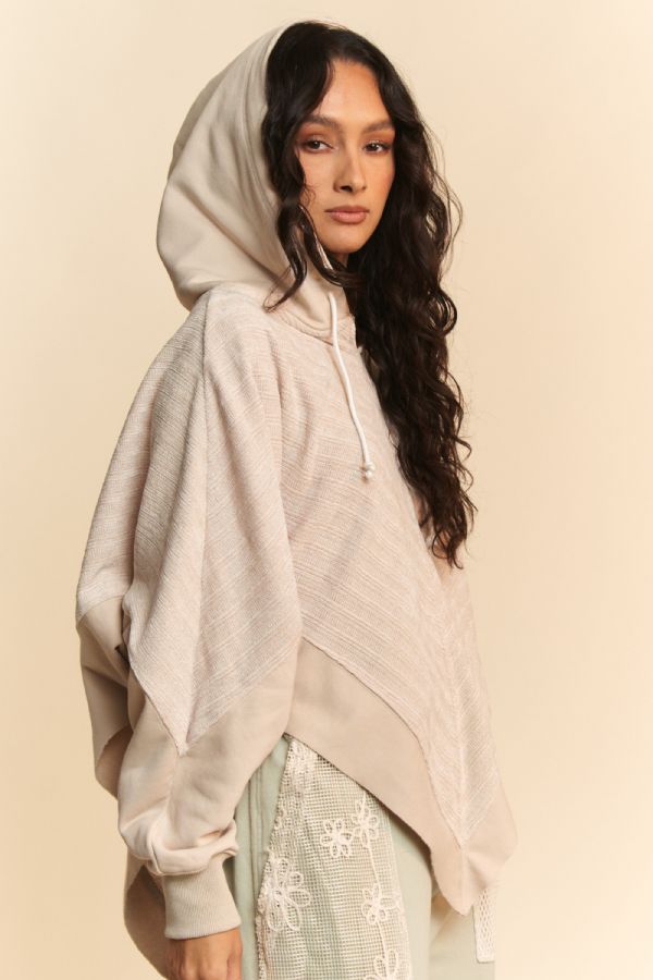 Woman wearing a beige hooded poncho over a light green outfit with floral patterns on a beige background