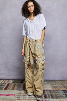 Woman wearing a light gray top and beige cargo pants against a gray wall.