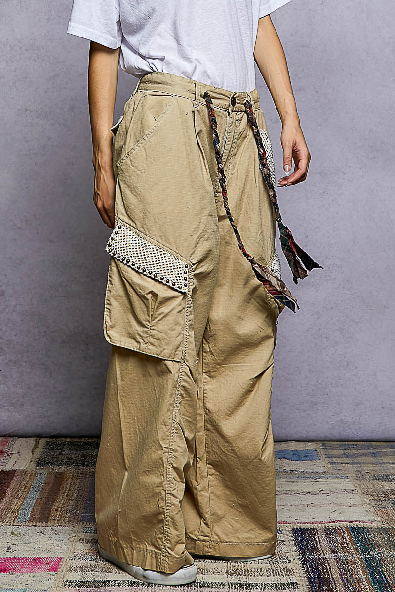 Person wearing beige cargo pants with decorative elements on a gray background