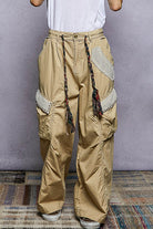 Beige cargo pants with decorative patches worn by a person against a plain background