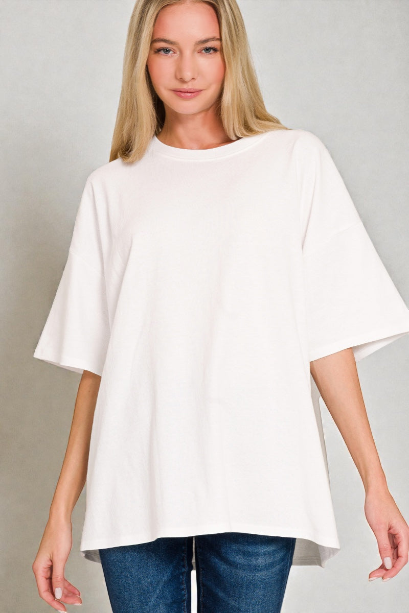 Woman wearing a white oversized top and blue jeans on a gray background