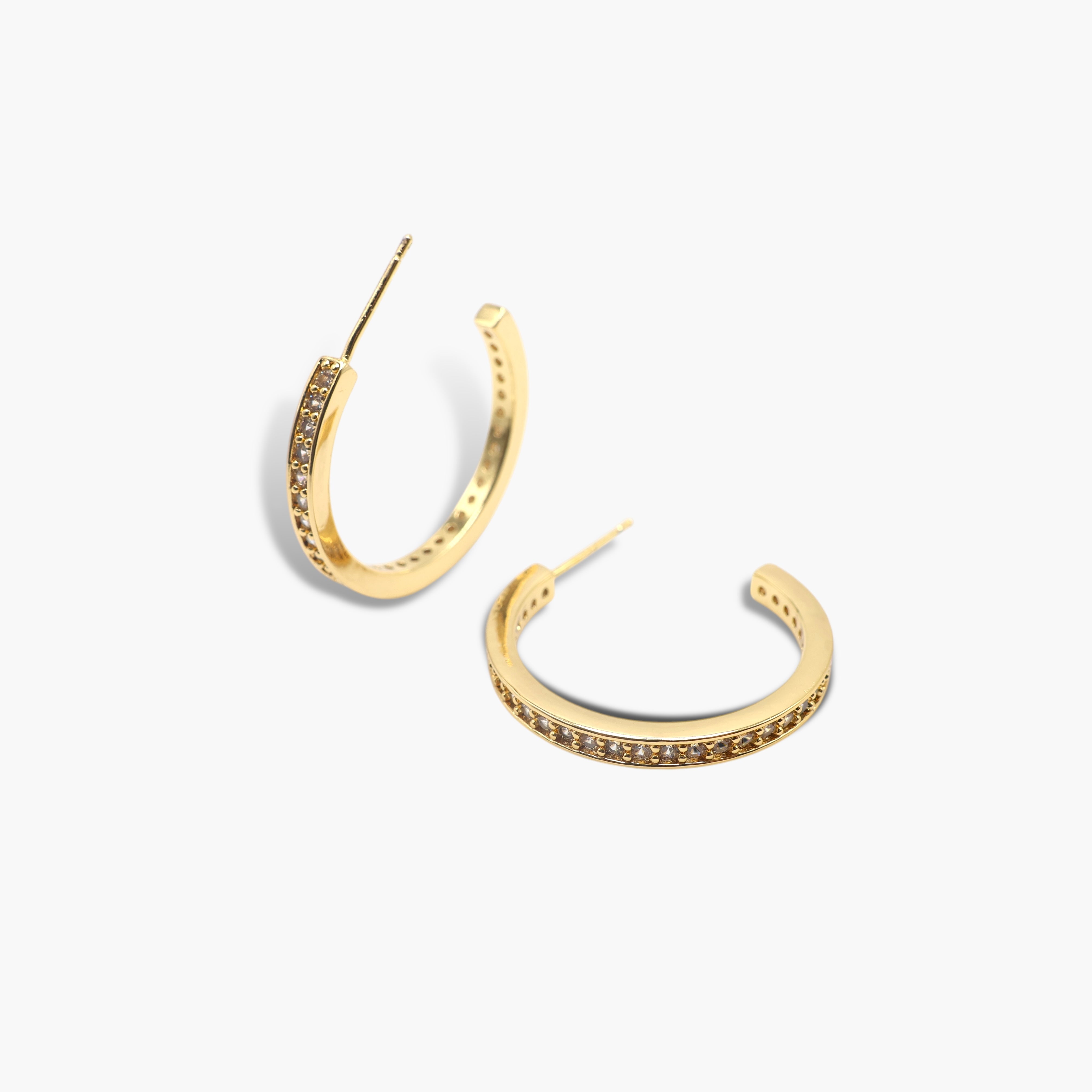 A pair of gold-colored hoop earrings with pave (small stones) on the hoop surface.