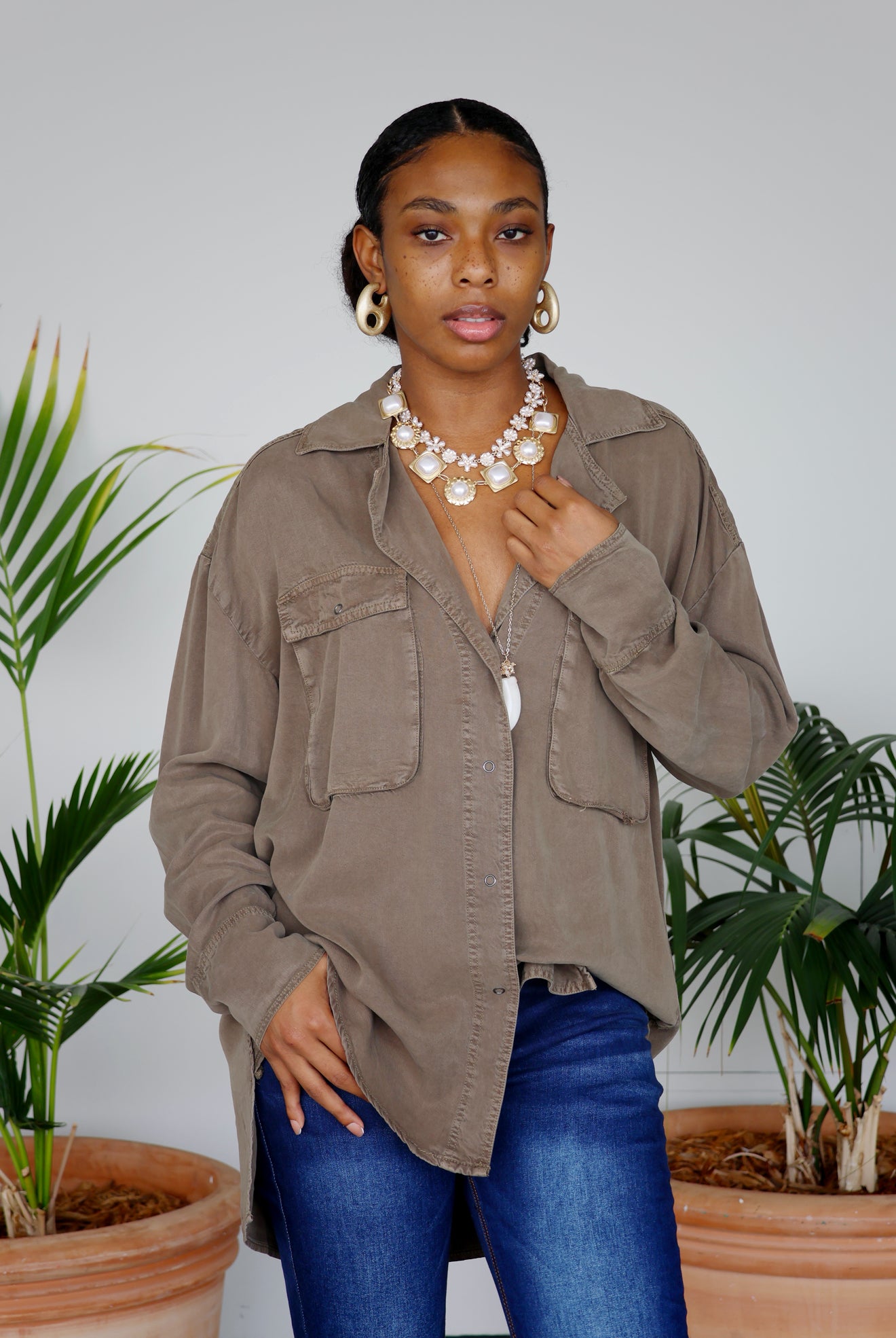 Woman wearing a brown jacket and blue jeans standing in front of plants
