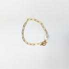Gold chain bracelet with a pearl charm on a light gray background
