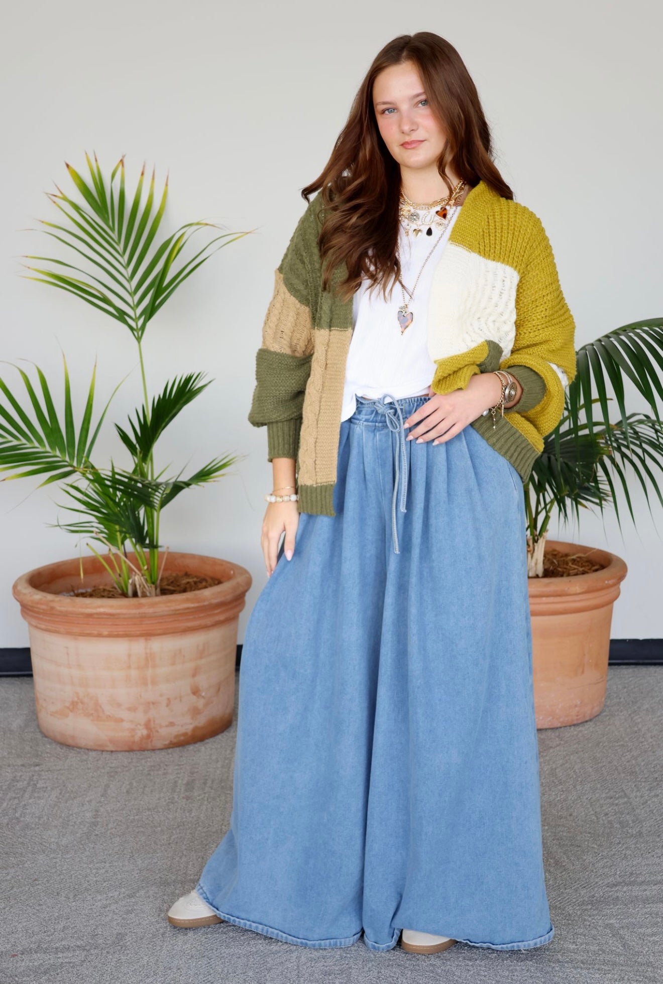 Woman wearing a colorful cardigan and blue pants standing in front of potted plants.