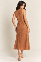 Brown sleeveless midi dress with an intricate textured pattern, subtle shimmer, and a flowing A-line silhouette, styled with layered pearl necklaces, bracelets, and nude strappy heels.