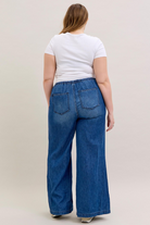 Person wearing blue wide-leg jeans and a white t-shirt on a beige background