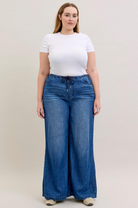 Woman wearing a white t-shirt and blue wide-leg jeans on a plain background