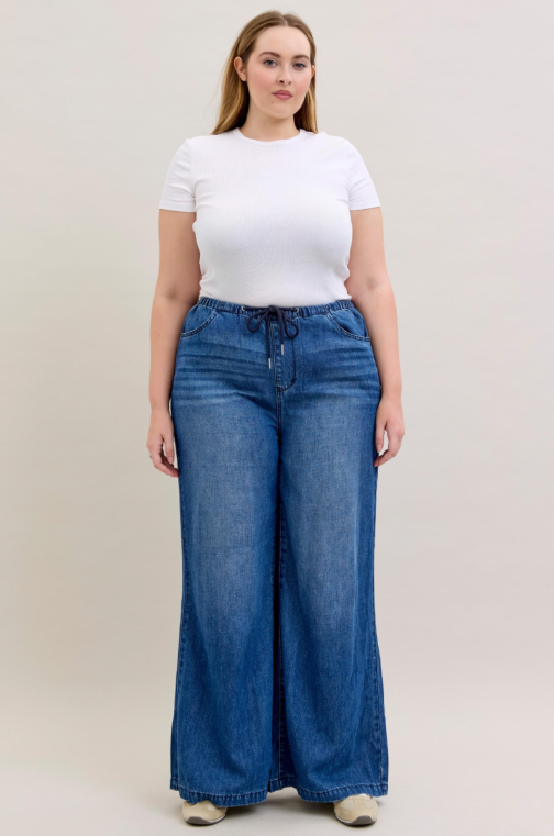 Woman wearing a white t-shirt and blue wide-leg jeans on a plain background