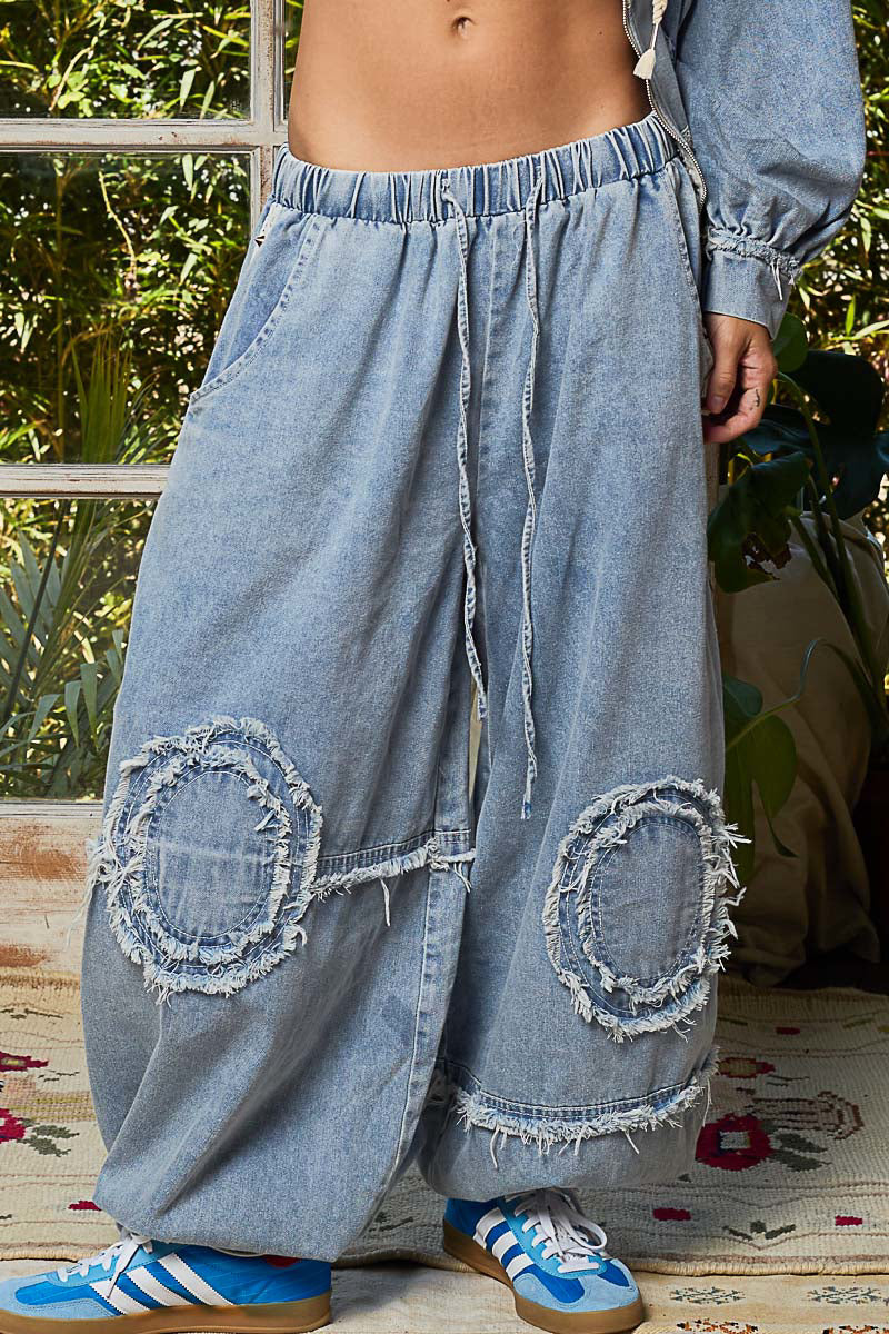 Person wearing light blue denim wide-leg pants with patches, standing outdoors.