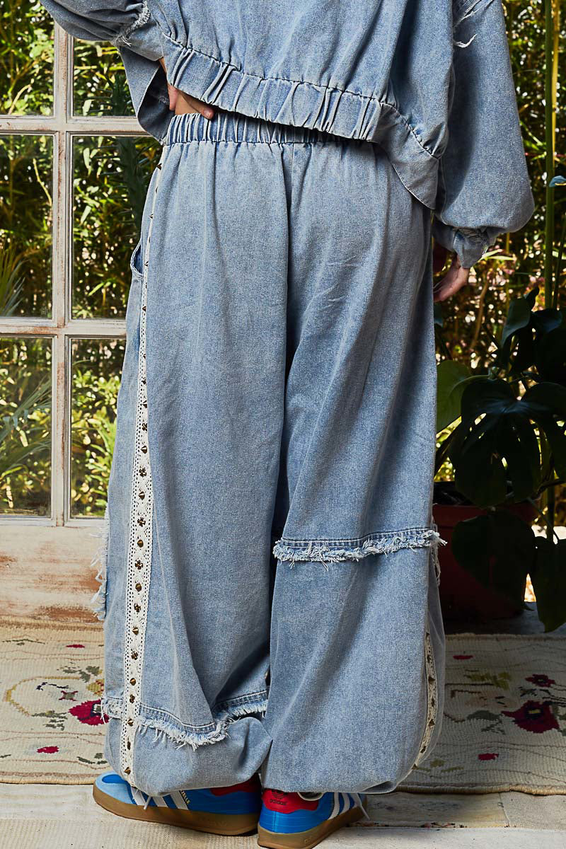 Person wearing a denim outfit with lace trim in a room with plants and a window.