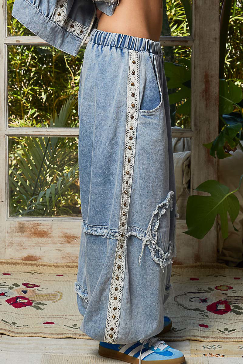 Person wearing a long denim skirt with lace details in a room with plants and a rug.