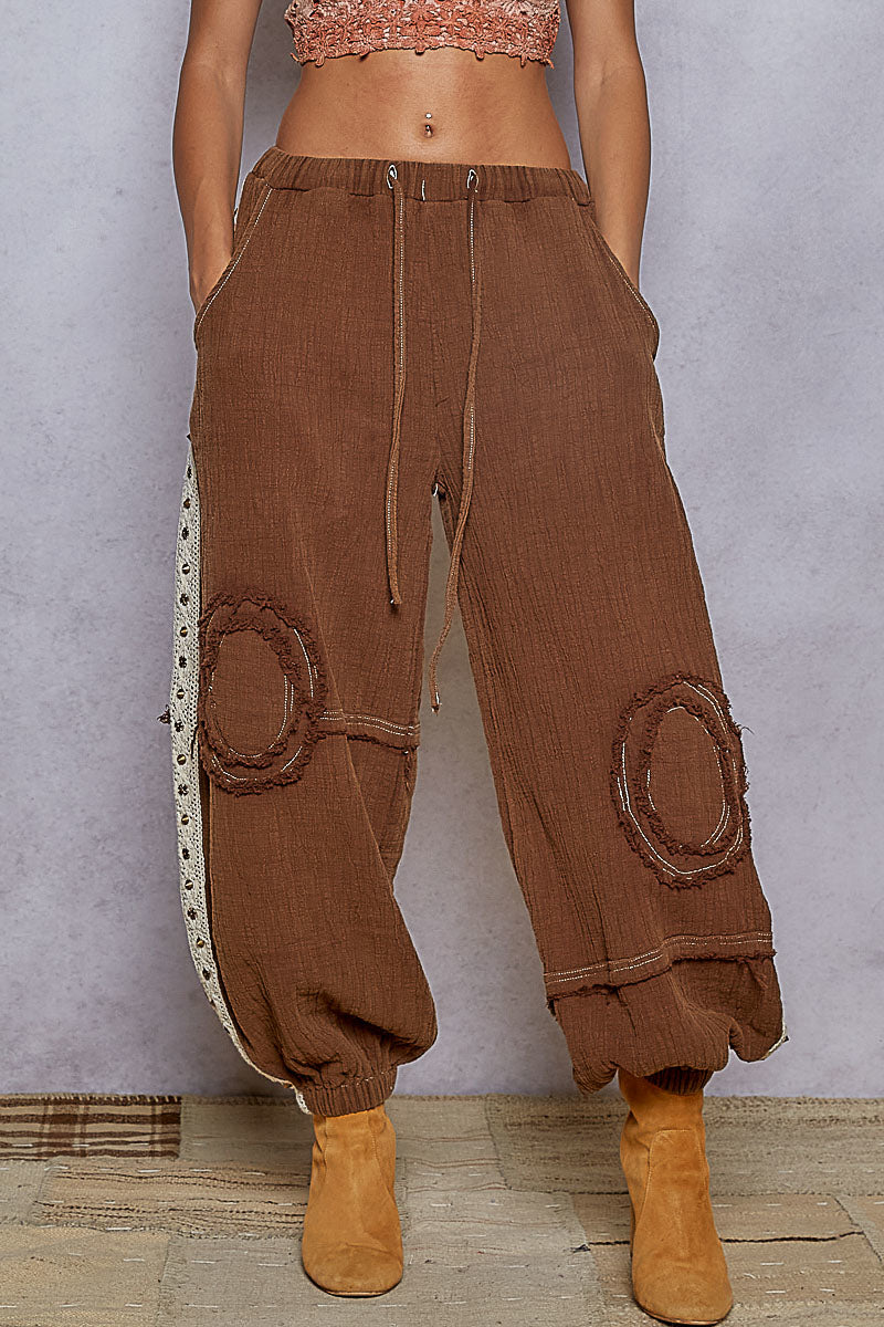Brown corduroy pants with decorative patches worn by a person against a neutral background