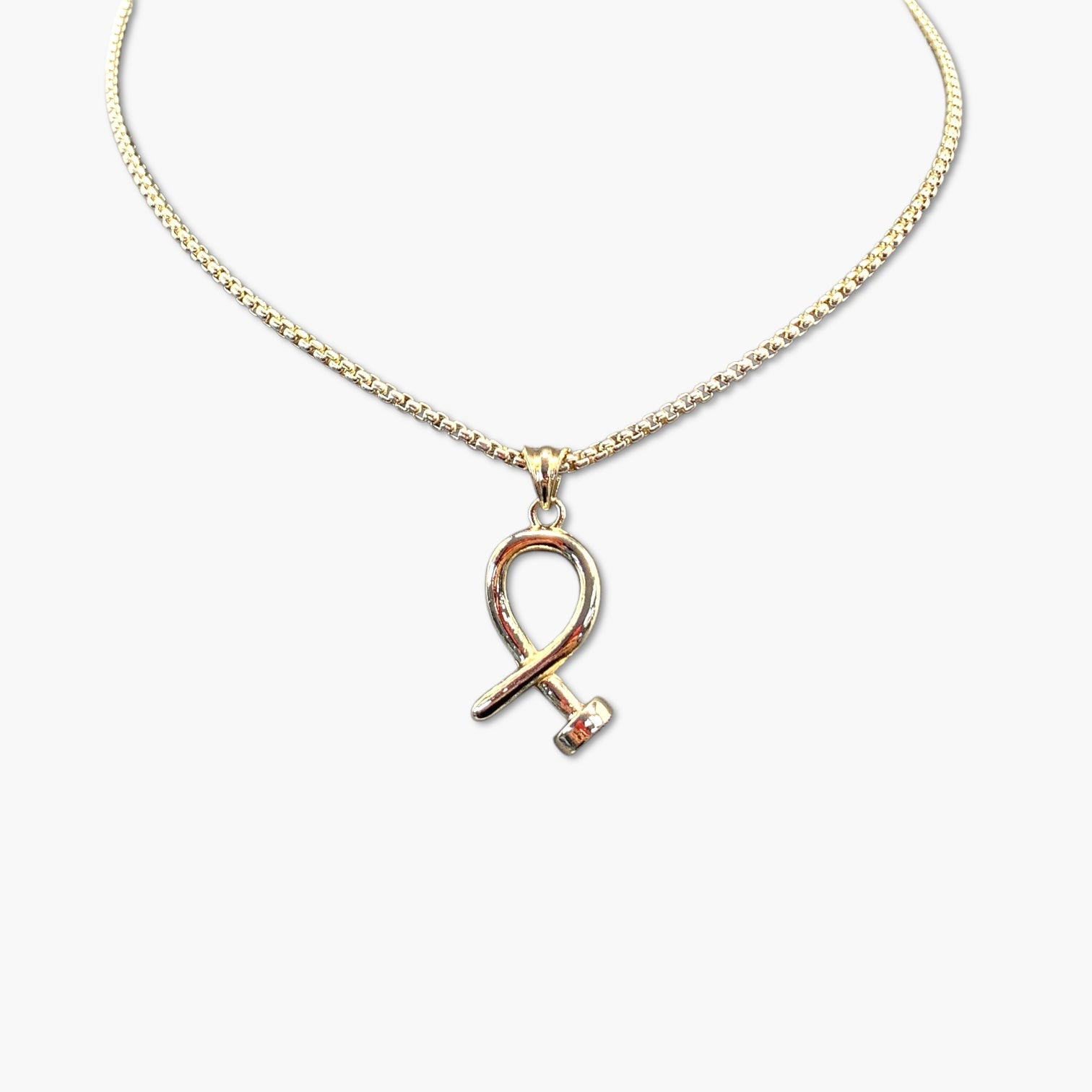 A gold-colored nail necklace with a bohemian and vintage style, featuring a ribbon-shaped charm on a chain.