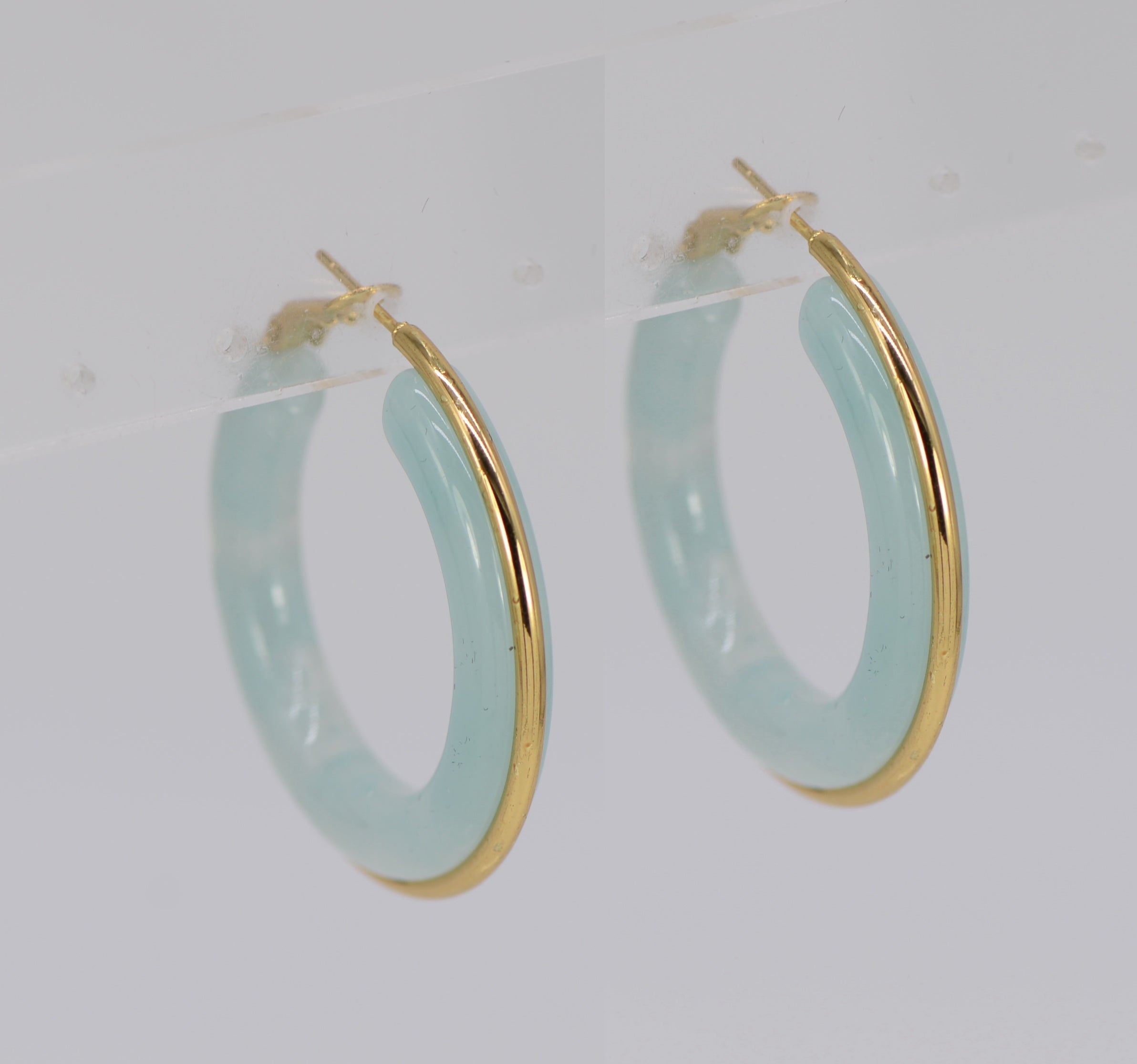 A pair of gold wrapped acrylic hoop earrings with a green marbled pattern.
