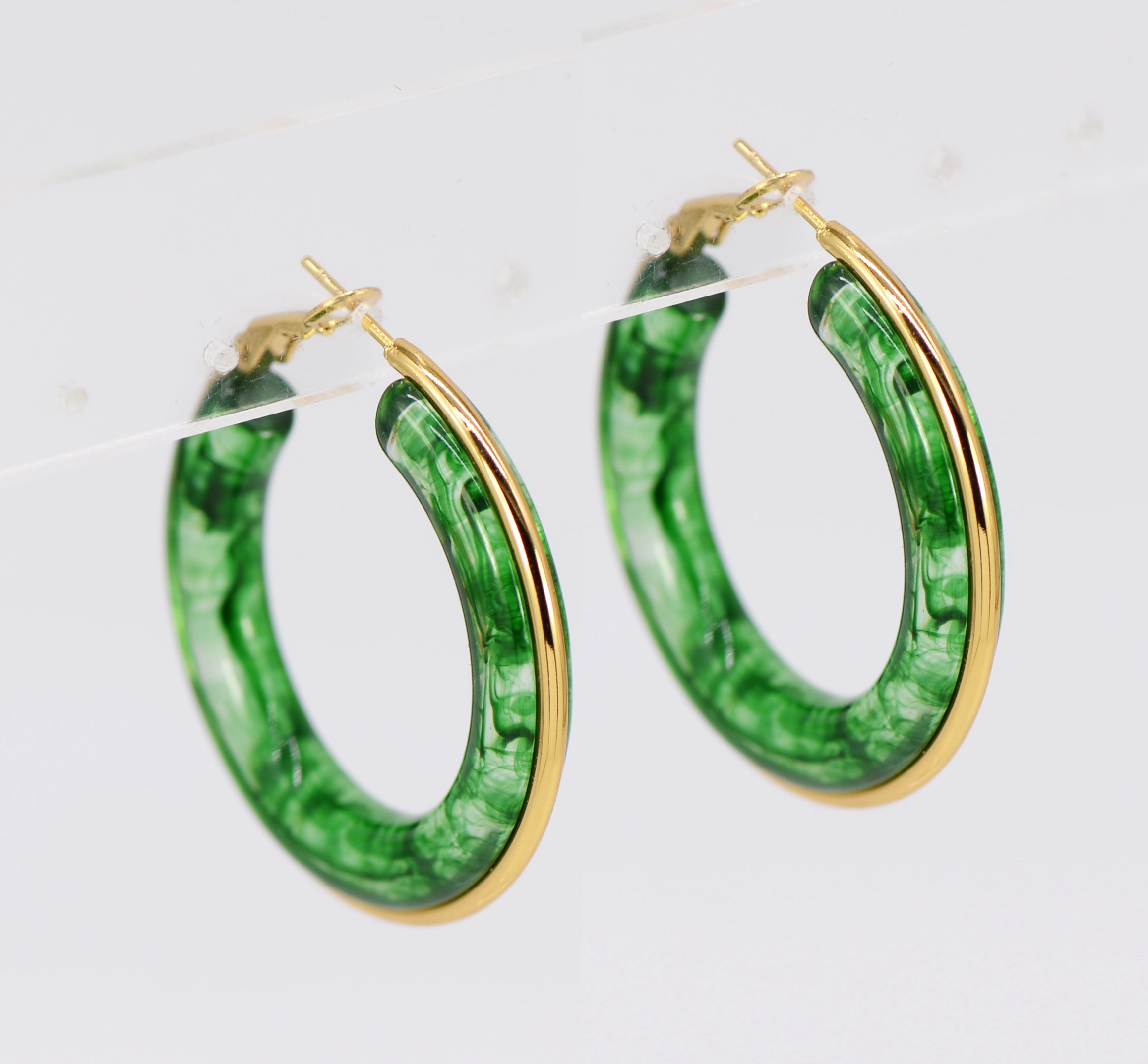 A pair of gold wrapped acrylic hoop earrings with a green marbled pattern.