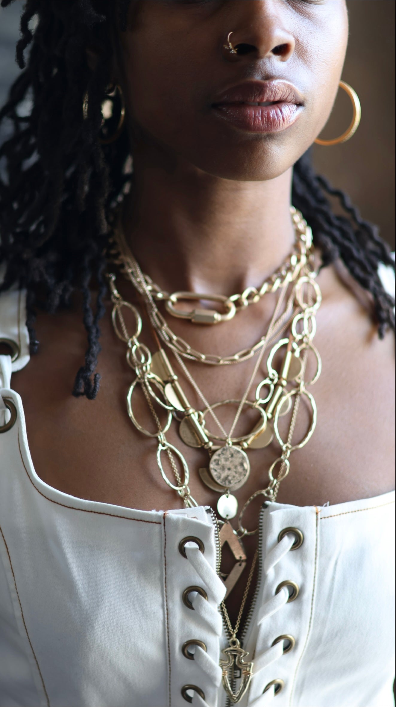 A person wearing a white laced top adorned with multiple gold-colored necklaces featuring various shapes and designs.