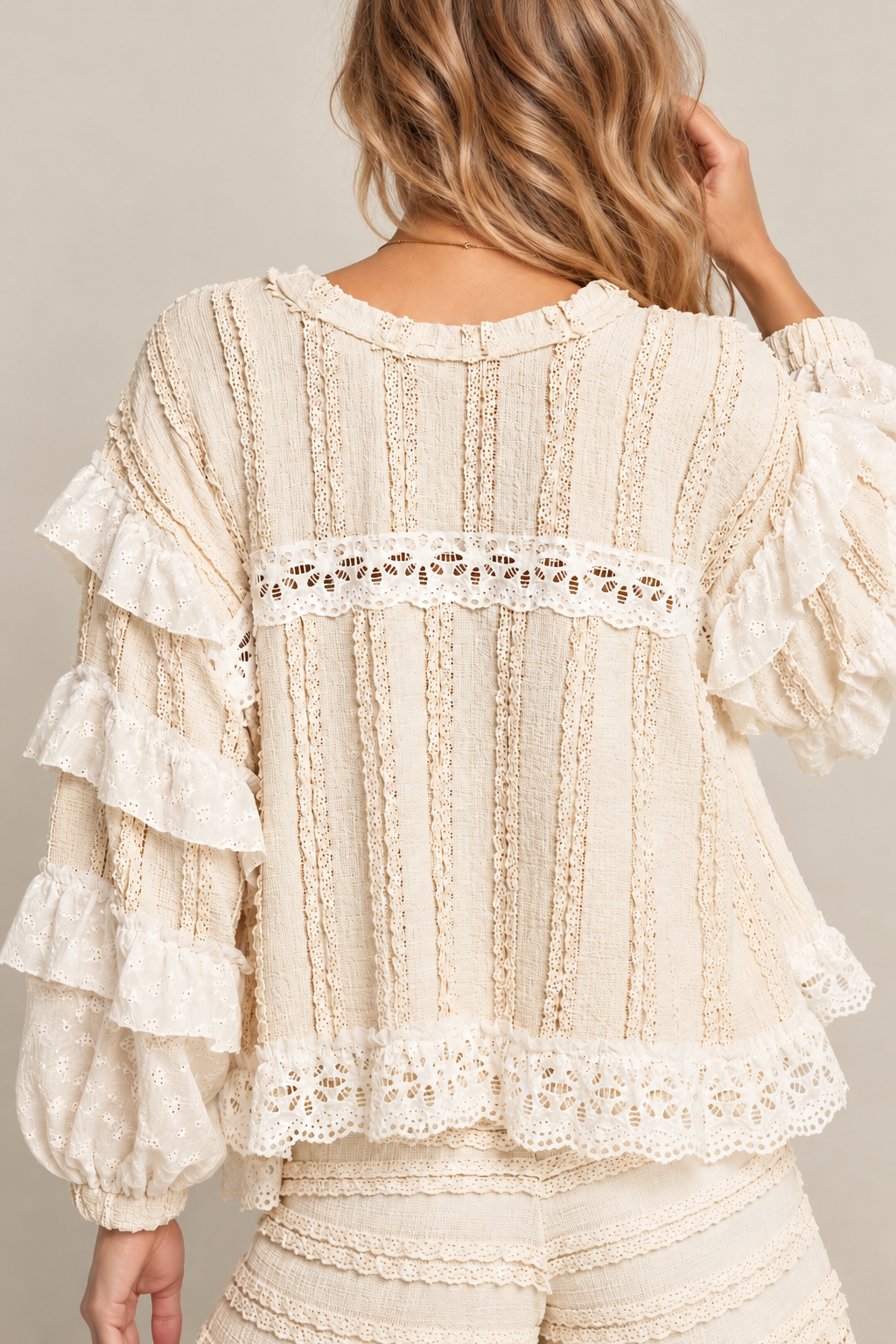 Back view of a model wearing a cream crochet lace blouse with ruffled sleeves and eyelet trim, paired with matching textured shorts.