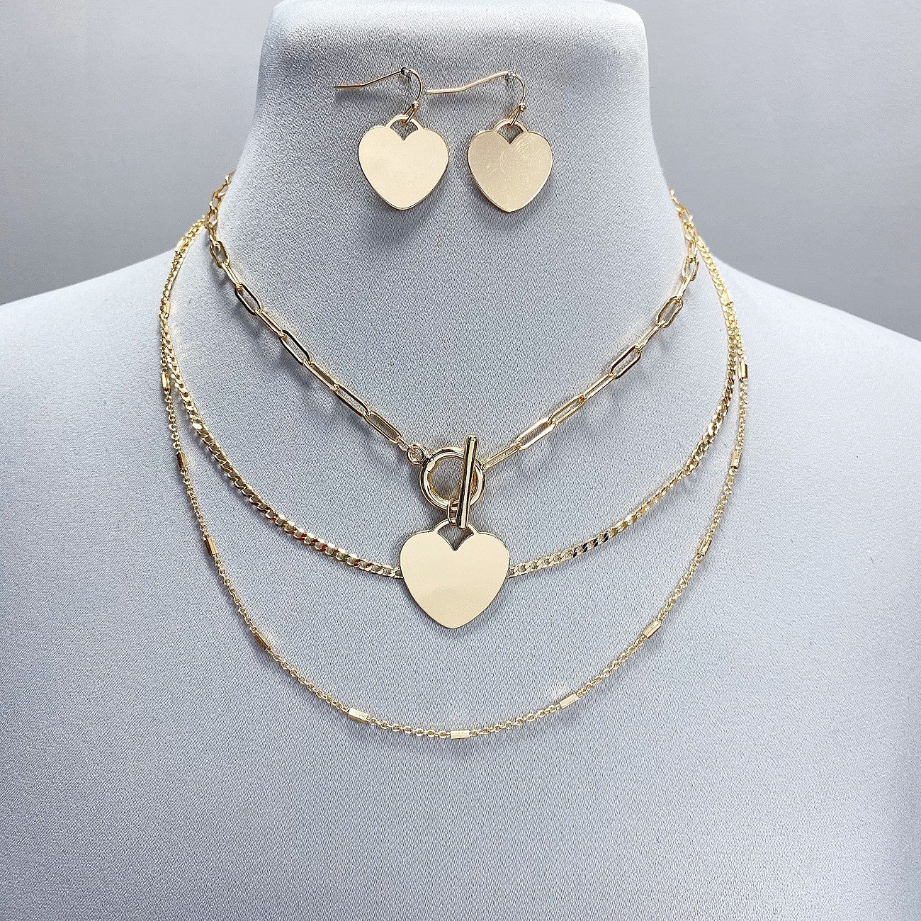 Gold heart-shaped necklace and earrings on a mannequin bust.
