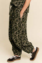 Person wearing leopard print pants with black sneakers on a beige background