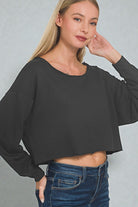 Woman wearing a black cropped sweatshirt and blue jeans against a gray background