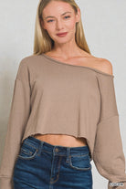 Woman wearing a brown off-shoulder top and blue jeans against a plain background