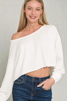 Woman wearing a white off-shoulder top and blue jeans against a plain background