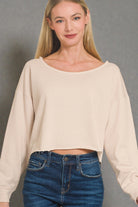 Woman wearing a beige sweater and blue jeans against a gray background