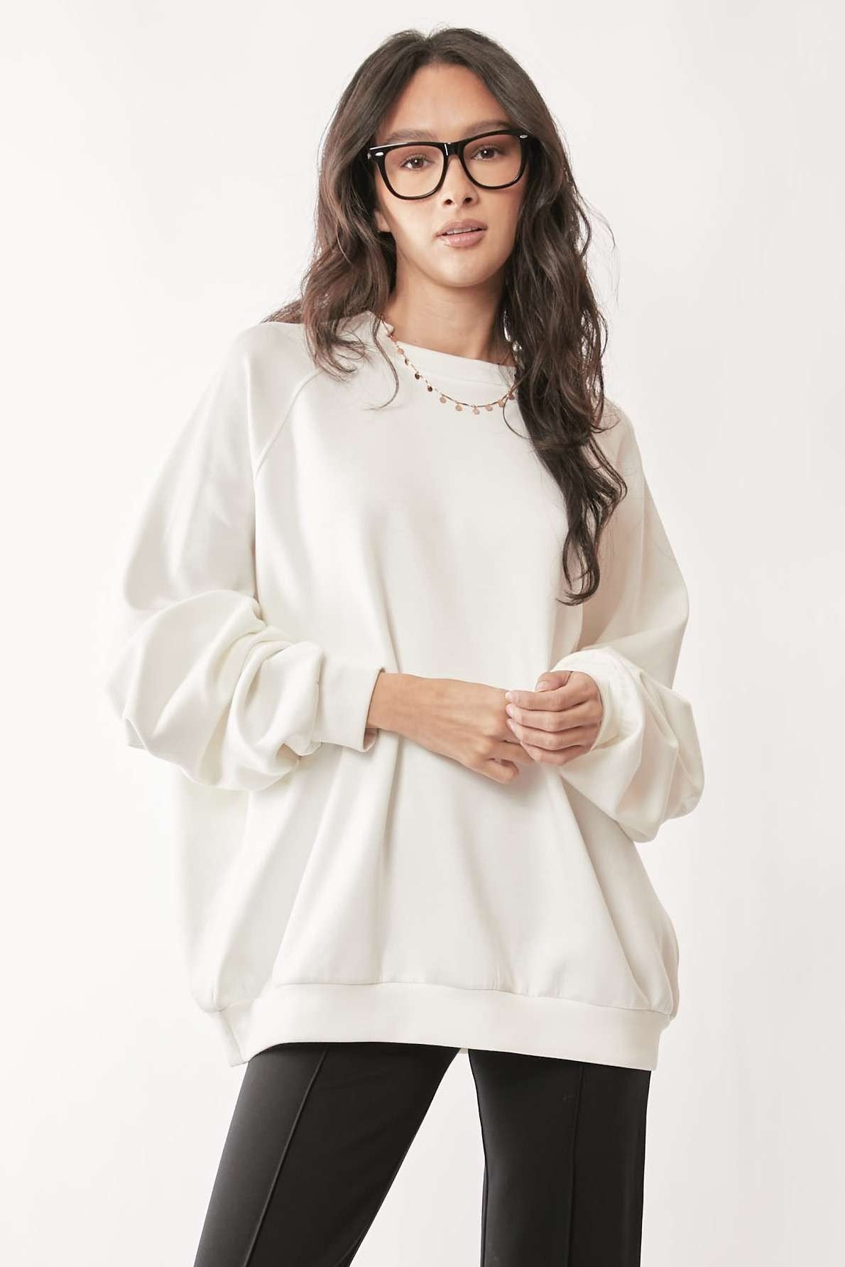 Woman wearing a white oversized sweatshirt and black pants on a white background