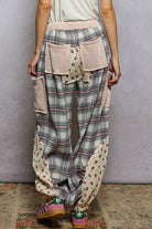 Plaid pants with floral patches worn by a person against a gray wall.