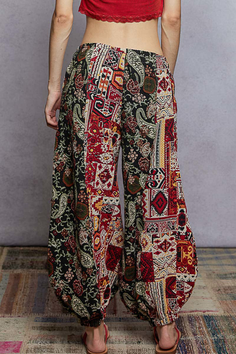 Person wearing colorful patterned pants with a red top on a plain background