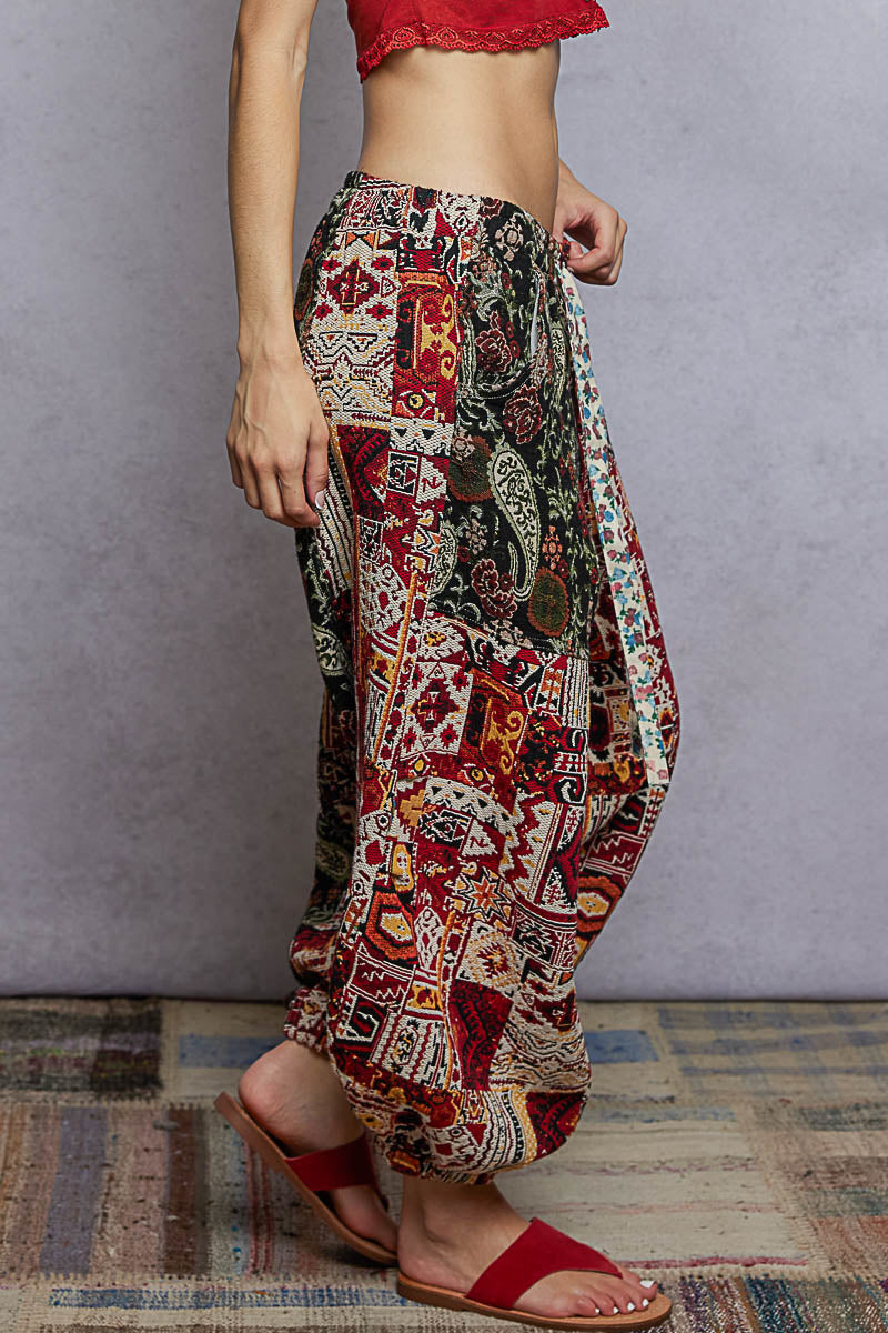 Person wearing colorful patchwork pants with a red top and sandals on a gray background