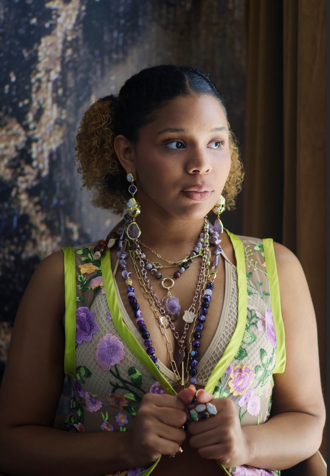 A person wearing multiple necklaces with amethyst stones and gold accents. The necklaces are part of a stack, and the person is holding some of the necklaces, showcasing the jewelry.
