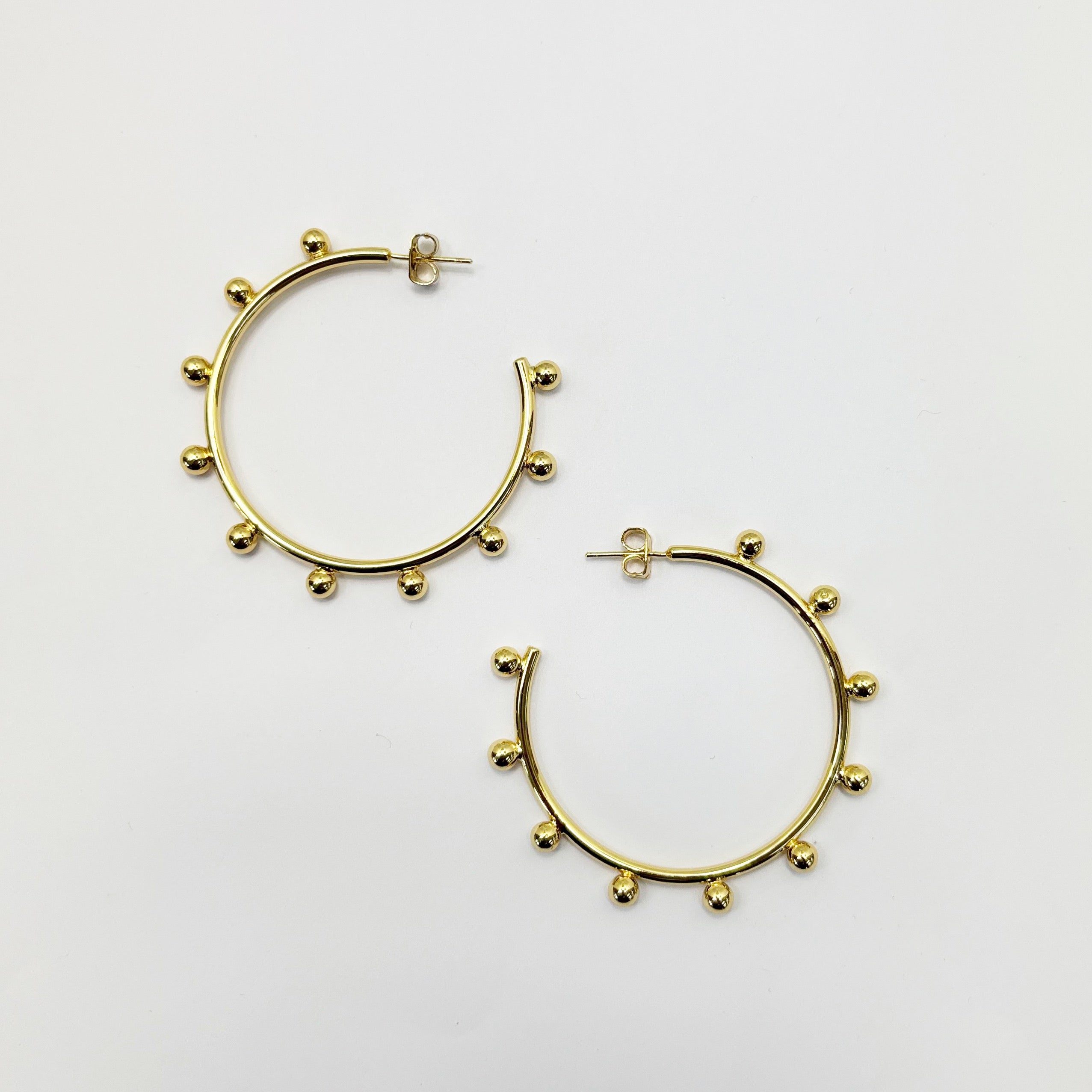 A pair of gold-colored hoop earrings with small ball design and silver posts on a white background.