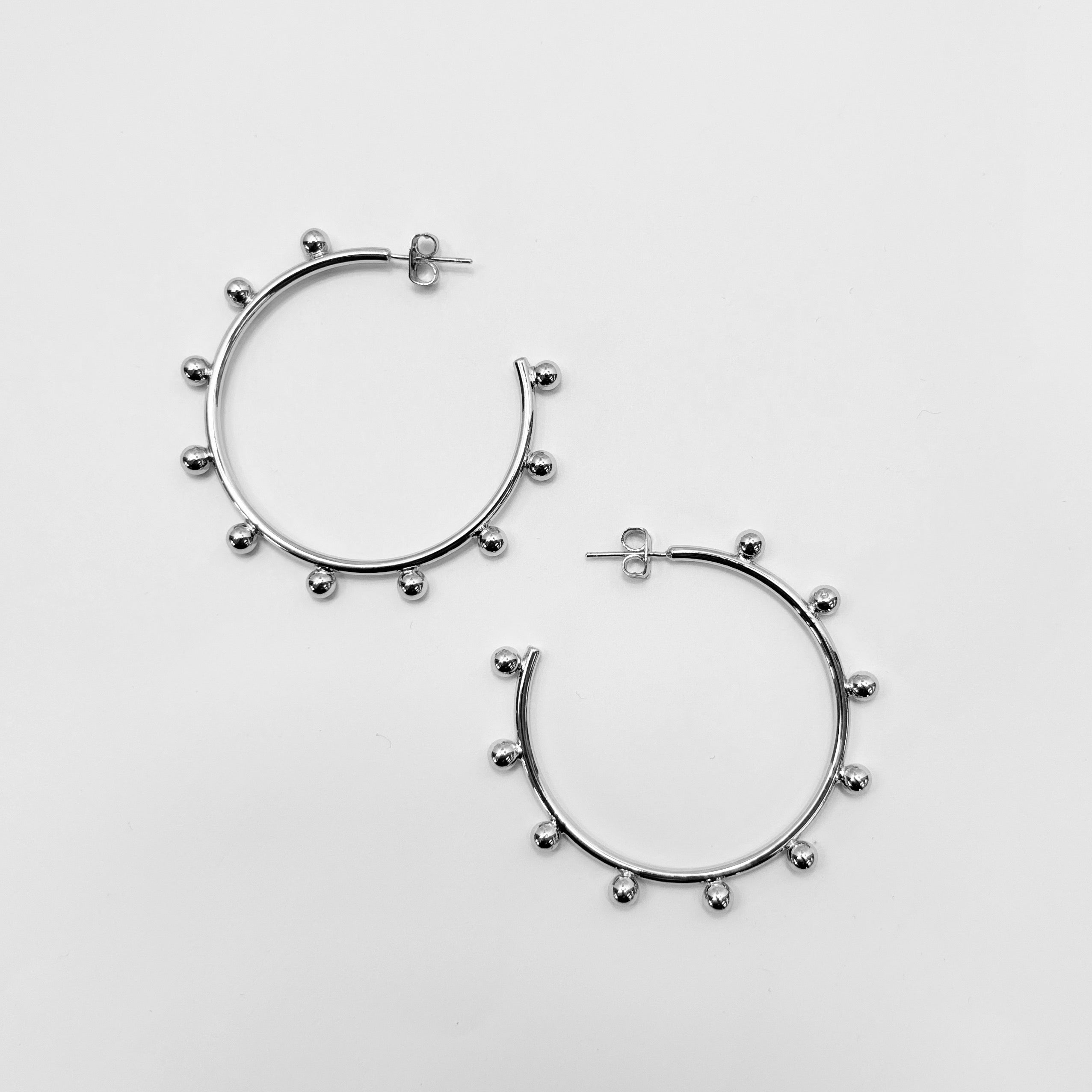 A pair of gold-colored hoop earrings with small ball design and silver posts on a white background.
