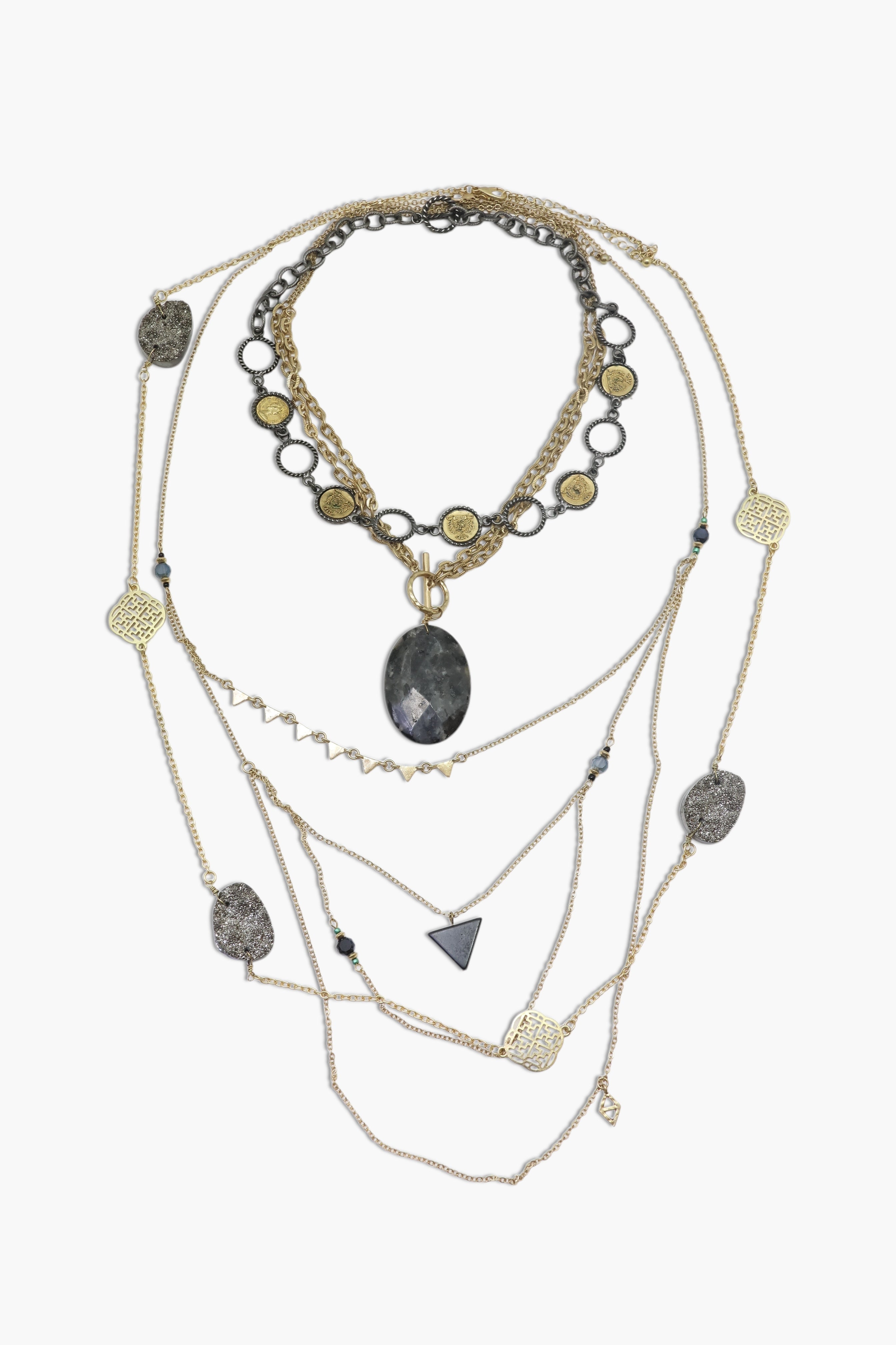 A layered necklace set with a variety of geometric pendants and a prominent central stone pendant, predominantly in shades of silver and gold.