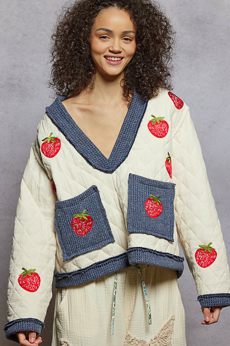 Woman wearing a cream sweater with red apple designs on a gray background