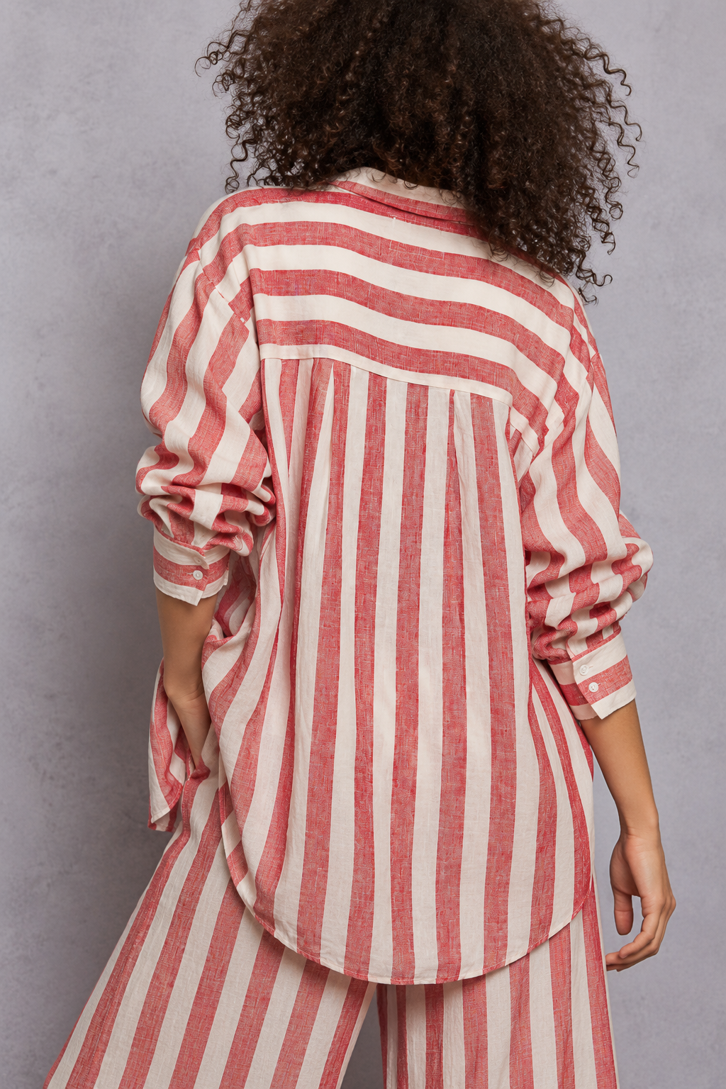 Red and white vertical striped button-down shirt with rolled sleeves, layered over a white lace-trim camisole and paired with matching striped pants, styled on a curly-haired model.