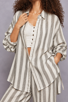 Grey and white vertical striped button-down shirt with rolled sleeves, layered over a white lace-trim camisole and paired with matching striped pants, styled on a model with curly hair.