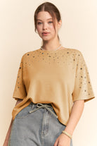 Woman wearing a mustard yellow top with black speckles and blue jeans on a beige background