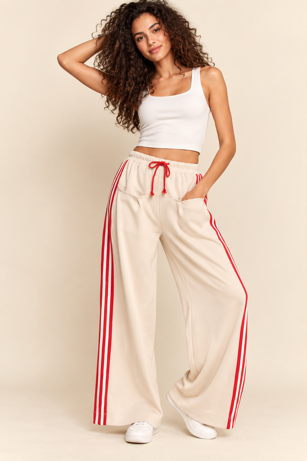 Cream wide-leg track pants with elastic waistband, red drawstring, front pockets, and bold red-and-white side stripes.