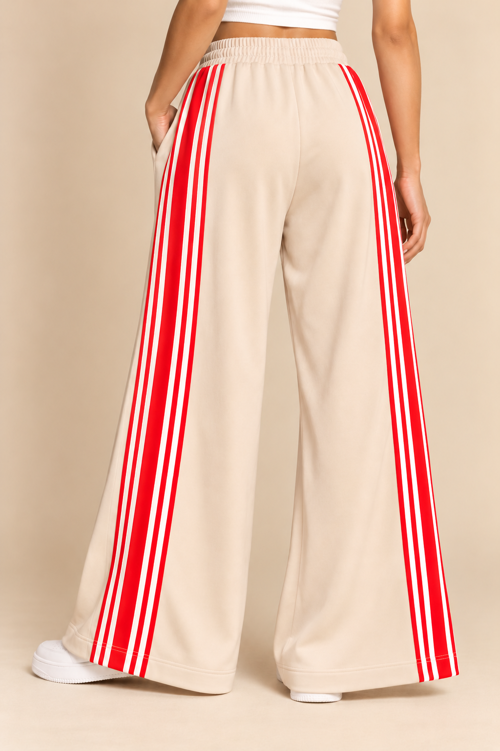 Cream wide-leg track pants with elastic waistband, red drawstring, front pockets, and bold red-and-white side stripes.