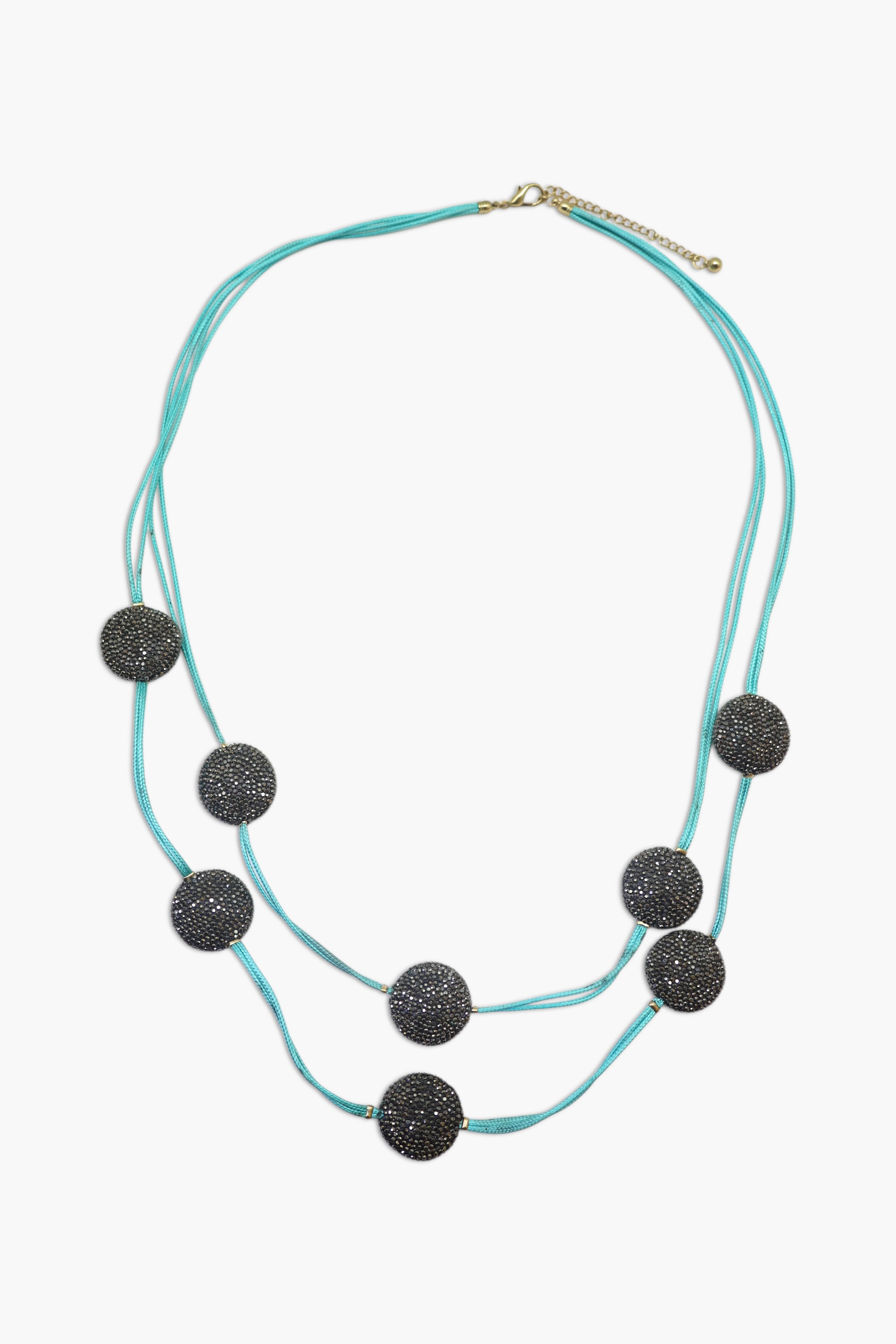 A woman wearing a turquoise and black stone necklace stack with matching earrings.