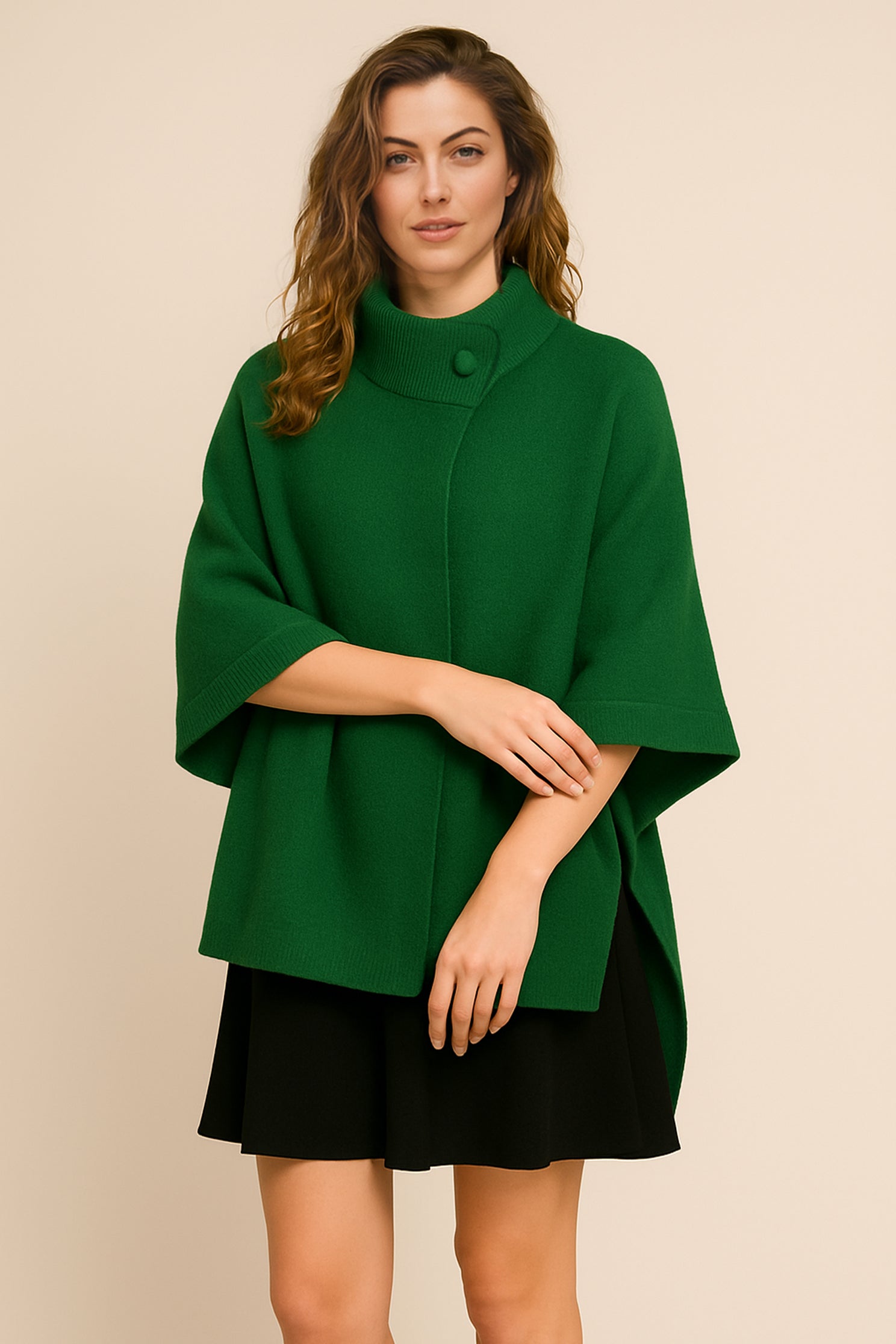 Woman wearing a green poncho over a black dress on a beige background
