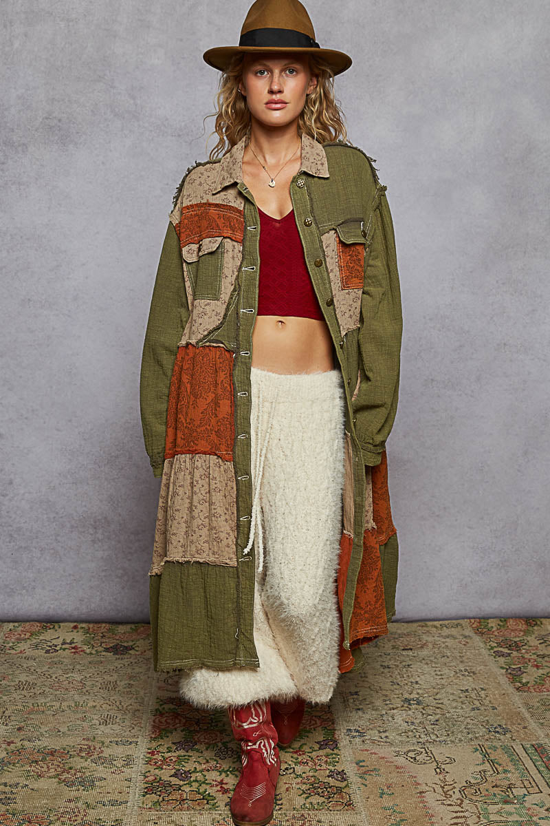Woman wearing a long, patchwork coat with a textured rug and plain wall background